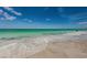 A serene beach scene features foamy waves gently rolling onto the light sand under a beautiful blue sky at 614 Gulf Blvd # 4, Indian Rocks Beach, FL 33785