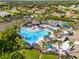 Aerial view of a large community pool with lounge areas, mature landscaping, and nearby tennis courts at 1319 Leland Dr # 101, Sun City Center, FL 33573