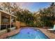 Backyard pool view highlighting a patio with cozy outdoor seating, lush landscaping, and evening lights at 235 Aberdeen St, Dunedin, FL 34698