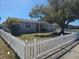 Street view of a home with a well-kept lawn, mature tree, and white picket fence at 3136 Primrose Dr, Holiday, FL 34691