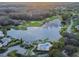 Gorgeous aerial view of a lakefront property featuring a pool, clubhouse, golf course and surrounding trees at 5473 Blue Heron Ln, Wesley Chapel, FL 33543