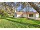 Lush green backyard featuring large shade trees, landscaped yard, and a glimpse of the terracotta roof at 5473 Blue Heron Ln, Wesley Chapel, FL 33543