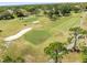 An aerial view of the golf course, featuring well-manicured green, mature trees, sand traps and players at 1489 Dundee Dr, Palm Harbor, FL 34684