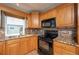 Well-lit kitchen featuring wooden cabinetry, granite countertops, tile backsplash, and black appliances at 19937 Gulf Blvd # B-3, Indian Shores, FL 33785