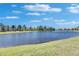 Scenic view of a lake surrounded by green grass and trees under a bright blue sky at 15657 Aurora Lake Cir, Wimauma, FL 33598