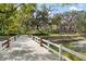 View of the beautiful brick house situated behind a white fenced bridge, lush trees and blue sky in background at 2906 Pemberton Creek Dr, Seffner, FL 33584