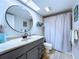 Bathroom with modern vanity, round mirror, and neutral tile flooring complemented by a patterned rug at 513 Hammock Pine Blvd, Clearwater, FL 33761