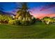 The home is nestled in lush landscaping with mature trees and bushes within a fenced yard at dusk at 6927 Crestpoint Dr, Apollo Beach, FL 33572