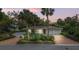 Charming home with well-manicured landscaping, a brick driveway, and mature palm trees against a colorful twilight sky at 201 Flamingo Dr, Belleair, FL 33756