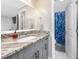 Bright bathroom featuring gray cabinets, granite countertops, and a view of the shower with a blue patterned curtain at 455 Alt 19 S # 162, Palm Harbor, FL 34683