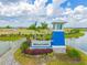 Landscaped entry sign for Bella Lago with blue tower, palm trees, flowers, and surrounding water at 10741 Charlotte Dr, Parrish, FL 34219