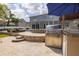 Outdoor kitchen with built-in grill and firepit, travertine patio, view of house, pool and seating at 4859 Augusta Ave, Oldsmar, FL 34677