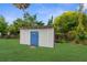 A backyard storage shed with a blue door is surrounded by grass and greenery at 9307 N 27Th St, Tampa, FL 33612