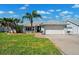 Well-maintained one-story home with a lush green lawn, palm trees, and attached two-car garage at 6410 3Rd Palm Pt, St Pete Beach, FL 33706