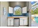 Outdoor kitchen featuring white cabinets, travertine floors, and tile backsplash overlooking the pool at 5384 Mira Vista Dr, Palm Harbor, FL 34685