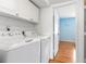 Bright laundry room featuring full-sized white washer and dryer with overhead cabinets and tile floor at 2646 Barksdale Ct, Clearwater, FL 33761