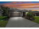 Home exterior showcasing a neutral color palette, well-manicured lawn, and a long driveway at dusk at 13001 Satin Lily Dr, Riverview, FL 33579
