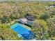 An aerial view of the property showcases the home's tennis court, pool, and large lot filled with mature trees at 2112 Laurence Dr, Clearwater, FL 33764