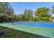 The blue and green tennis court is surrounded by mature trees and lush landscaping at 2112 Laurence Dr, Clearwater, FL 33764