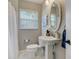 A neutral colored bathroom includes a pedestal sink, an oval mirror and natural light at 609 Osceola Rd, Belleair, FL 33756