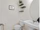 Clean half-bathroom with a pedestal sink, toilet, wall art, and black floating shelves on bright white walls at 12377 Streambed Dr, Riverview, FL 33579