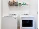 Bright laundry room with modern white washer and dryer beneath a shelf for storage and organization at 17533 Timberline Pkwy, Punta Gorda, FL 33982