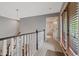 A brightly lit hallway featuring carpeted floors, a window with wooden blinds, and white wood trim around doors and railings at 27625 Lincoln Pl, Wesley Chapel, FL 33544