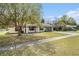 Single-story home featuring a lush front lawn and a mature shade tree, next to a concrete walkway at 38604 Camden Ave, Zephyrhills, FL 33540