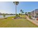 Expansive backyard with lush lawn, mature palm trees, and brick-lined landscaping, leading to a tranquil lakeside view at 1123 Signature Dr, Sun City Center, FL 33573