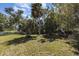 Spacious grassy backyard with mature trees, a fire pit, and partial white picket fence under a sunny, partly cloudy sky at 311 Ravenna N St, Nokomis, FL 34275