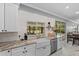 Well-lit kitchen featuring white cabinets, granite countertops, and a farmhouse sink with a view of the backyard at 15618 Shoal Creek Pl, Odessa, FL 33556