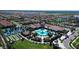 This aerial view shows the community center with a pool, well-manicured lawns and landscaping, tennis courts, and bocce ball at 17418 Holly Well Ave, Wimauma, FL 33598