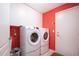Bright laundry room featuring modern, front-loading washer and dryer, ample white cabinetry, and red accent wall at 1308 Crystal Greens Dr, Sun City Center, FL 33573