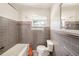 Bathroom with gray tile, tub, toilet, and window letting in natural light at 14040 Miramar Ave, Madeira Beach, FL 33708
