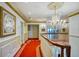 Elegant hallway featuring decorative chandelier, wainscotting, and patterned red carpet at 802 Druid S Rd, Clearwater, FL 33756
