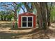 A charming red shed with white trim sits nestled among the trees in the backyard at 26290 Hayman Rd, Brooksville, FL 34602