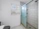 Bathroom featuring a glass shower with white tiles, a gray floor, white walls, and a window with white shutters at 13982 Whisperwood Dr, Clearwater, FL 33762