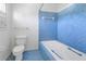 Bathroom with toilet, white tub, blue tile, and white walls with window and a towel rack at 13982 Whisperwood Dr, Clearwater, FL 33762