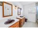 Bathroom with double vanity, wooden cabinets, mirrors, fixtures, white walls, and a window with white shutters at 13982 Whisperwood Dr, Clearwater, FL 33762