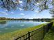 Scenic view of a community pond reflecting the sky, framed by lush greenery and a wrought iron fence at 30423 Ceasar Park Dr, Wesley Chapel, FL 33543