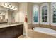 Bright bathroom featuring double windows, a soaking tub, and a granite countertop vanity at 3198 Thatcher Ln, Tarpon Springs, FL 34688