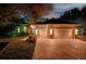 Elegant home showcasing a three-car garage, brick driveway, and lush landscaping illuminated at night at 3198 Thatcher Ln, Tarpon Springs, FL 34688