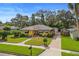 Charming yellow home featuring a well-manicured front yard, striped awnings, and brick-paved driveway at 225 Garden S Cir, Dunedin, FL 34698