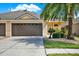 Charming one-story home featuring a two-car garage, a well-manicured lawn, and tropical landscaping with mature palm trees at 31833 Turkeyhill Dr, Wesley Chapel, FL 33543