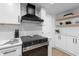 Close up of kitchen featuring stainless steel oven, hood, white cabinets, and floating shelves at 3352 Honeymoon Ln, Holiday, FL 34691