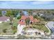 Stunning aerial view of a red-roofed home with a fountain, lush landscaping, and a picturesque lake backdrop at 4404 Lake In The Woods Dr, Spring Hill, FL 34607