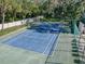 Aerial view of a fenced in community tennis court with blue surface, set in a wooded area at 1908 Bayshore Ct, Safety Harbor, FL 34695