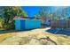 A detached shed with a solid blue door, surrounded by mature trees and a cracked concrete foundation at 860 16Th S Ave, St Petersburg, FL 33701