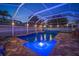 A well-lit backyard pool area with a brick floor, covered enclosure, and privacy fence for nighttime enjoyment at 513 Manns Harbor Dr, Apollo Beach, FL 33572
