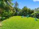 Spacious backyard featuring a grassy lawn, palm trees, mature trees, and fire pit with chairs at 13420 Rustic Pines S Blvd, Seminole, FL 33776